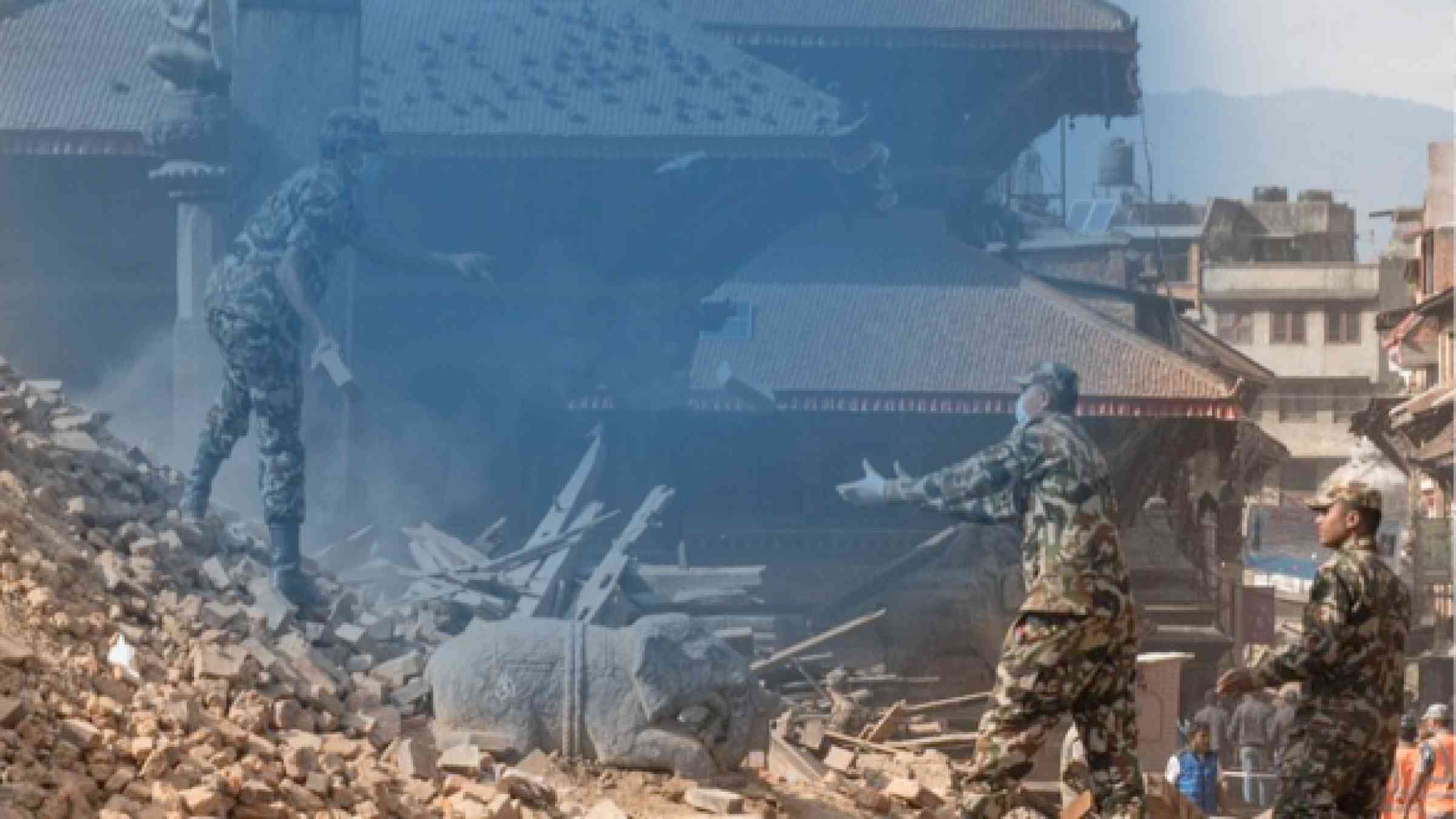 An image of three soldiers helping to clean up on a pile of rubble bricks in front of destroyed homes 